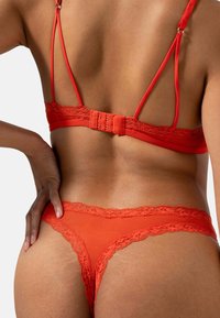 Ensemble de lingerie en dentelle rouge comprenant un soutien-gorge avec des bretelles ajustables et une fermeture à crochet, accompagné d'un string assorti avec des bordures en dentelle.