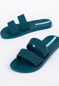 Sandali in gomma turchese con due fasce intrecciate, suole texturizzate e un accento blu chiaro. Progettati per il comfort e per essere antiscivolo.
