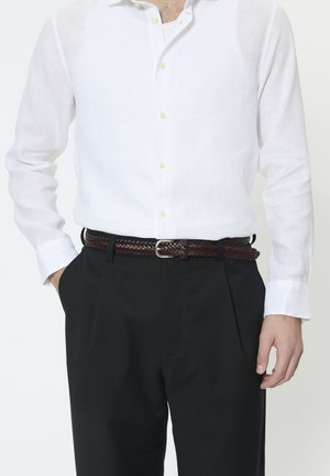 Weißes Leinenshirt mit langen Ärmeln und goldenen Knöpfen, kombiniert mit schwarzen Hosen und einem braunen, geflochtenen Ledergürtel mit silberner Schnalle.