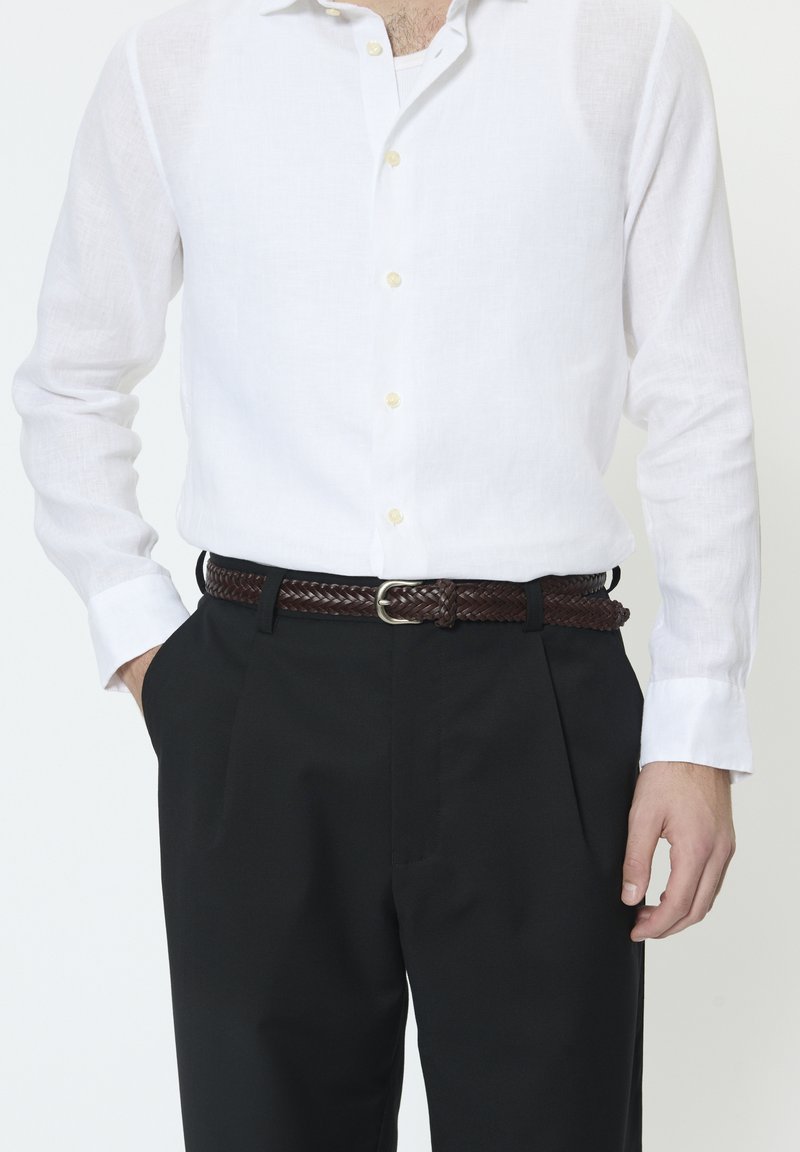 Bela lanena srajca z dolgimi rokavi in zlatimi gumbi, združena s črnimi hlačami in rjavim tkanim usnjenim pasom s srebrno sponko.