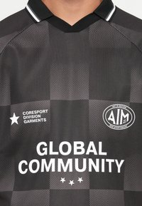 Μαύρο και γκρι καρό αθλητικό πουκάμισο με λευκό κείμενο "GLOBAL COMMUNITY" και λογότυπα "CORESORT DIVISION GARMENTS" και "AIM New Sportswear."