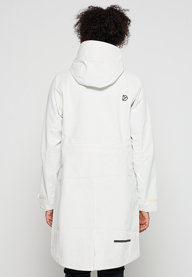 Person in einem langen weißen Kapuzenjacke mit einem kleinen schwarzen Logo auf dem oberen Rücken und einem schwarzen horizontalen Streifen am Saum.