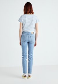 T-shirt de manga curta azul e branca com riscas, acompanhado de jeans de cintura alta de azul claro e ténis brancos com detalhes em amarelo e roxo.