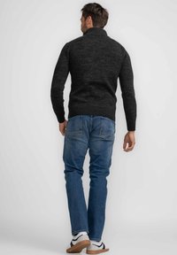 Donkergrijze gebreide trui met een hoge kraag, geribbelde zoom en aansluitende mouwen, gecombineerd met lichtblauwe denim jeans en casual schoeisel.