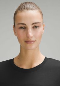 Musta lyhythihainen paita, jossa on ribattu pyöreä kaula-aukko, sileä pintakangas ja hienovarainen muotoilu, jota henkilö pitää neutraalilla taustalla.