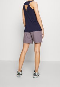 Marint ärmlös topp med en nyckelhålsdesign på baksidan, matchad med ljusgrå shorts. Modellen har på sig grå och svarta sportskor med en texturerad sula.