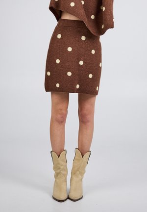 Jupe en tricot marron à pois crème, associée à un haut assorti et des bottes de cowboy beiges.