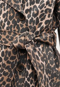 Παλτό τύπου trench με λεοπάρ μοτίβο σε μπεζ και μαύρο, με υφασμάτινη ζώνη στη μέση, δύο κουμπιά και υφή στην επιφάνεια.