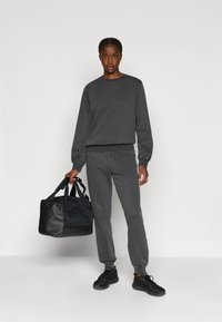 Hallhalli puuvillane ümmarguse kaeluse dressipluus ja vastav jalgpükste komplekt, millele on lisatud must duffel kott ja mustad tossud. Lihtne, funktsionaalne disain.