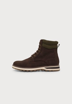 Botte en daim marron foncé à lacets avec col matelassé olive, semelle rayée beige et noire, et semelle extérieure robuste.