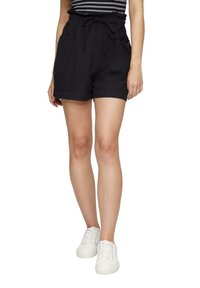 Shorts noirs taille haute avec une taille élastique à cordon, dotés de poches avant, d'un ourlet roulé et d'une texture de tissu douce. Associés à des baskets blanches.