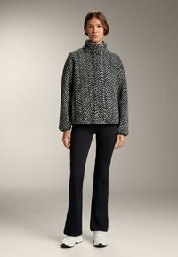 Kurtka w czarno-białą strukturę w jodełkę z wysokim kołnierzem, opadającymi ramionami i luźnym krojem, w połączeniu z czarnymi spodniami w kształcie dzwonów i trampkami.