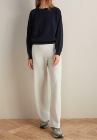 Mörkblå tröja med långa ärmar, rund halsringning, mjuk textur. Vita byxor med vida ben i avslappnad passform, tillsammans med grå sneakers.