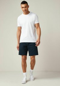 Camiseta de algodón blanca combinada con pantalones cortos azul marino, con un corte recto. El modelo lleva zapatillas blancas y calcetines hasta el tobillo.