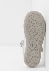 Sandale argentée avec une semelle en caoutchouc texturé et flexible, ornée d'un motif floral, et une sangle Velcro pour un maintien sécurisé. Taille 25 visible.