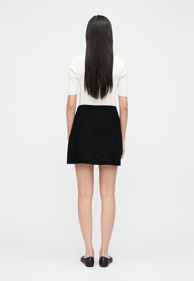 Black suede skirt with a straight cut, worn with a fitted white top. The model's long hair is straight, and she is facing away from the viewer.