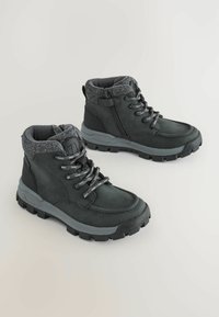Bottes de randonnée noires avec tige texturée, fermeture à lacets, collier rembourré et semelle en caoutchouc avec crampons agressifs pour une meilleure adhérence.