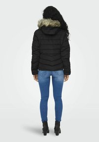 Padded svart jakke med hette fôret med pels, med et chevron-søm mønster på ryggen. Båret med blå skinny jeans og svarte ankelstøvler.