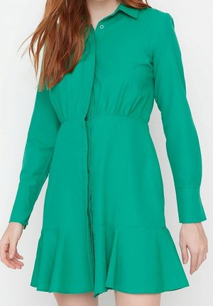 Robe verte à boutons faite d'un tissu lisse. Elle présente un corsage ajusté, une taille froncée, des manches longues et un ourlet évasé.