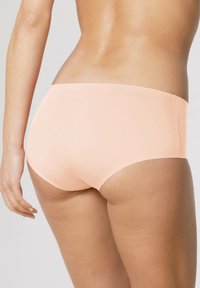 Culottes de couleur pêche, unies, avec une texture lisse et une taille mi-haute, dotées d'une ceinture simple et d'une couverture intégrale à l'arrière.