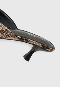 Talons noirs avec une sangle en imprimé serpent, présentant une forme incurvée et une finition brillante. Matériau texturé et design épuré.