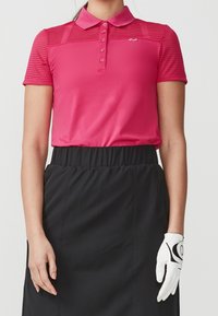 Rosa polo skjorta med randigt mönster, fem knappar och krage, kombinerad med en svart kjol. Vit golfhandske på vänster hand med svarta accenter.