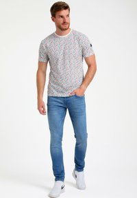 Ti-shirt kuvioilla, valmistettu kevyestä kankaasta, jossa on monivärinen muotoilu. Yhdistetty sinisiin farkkuihin ja valkoisiin lenkkarit.
