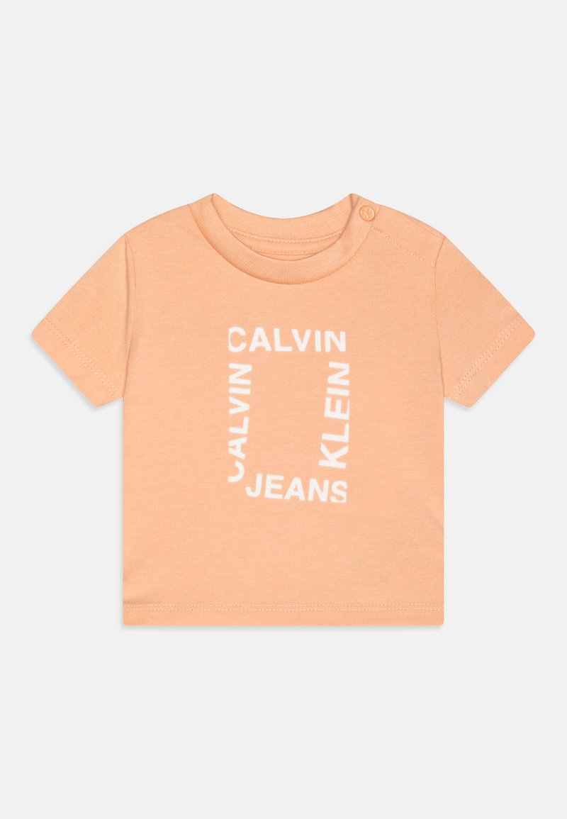 T-shirt de manga curta em pêssego claro, feito de algodão, com uma impressão de logotipo branca com 'CALVIN KLEIN JEANS' em um design retangular. Botão de pressão no ombro.