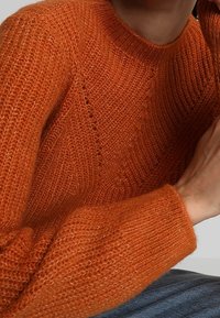 Pull tricoté orange avec un motif texturé et un col côtelé. Vue en gros plan mettant en avant la douceur du tissu et les détails.
