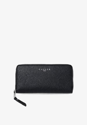Cartera negra Gaëlle Paris de piel granulada, con cremallera perimetral y correa para la muñeca, sobre un fondo blanco.