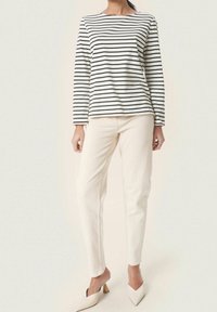 Gestreiftes langärmliges Oberteil in Schwarz und Weiß, kombiniert mit cremefarbenen Hosen. Die Mules haben eine spitze Zehenpartie und einen kleinen Blockabsatz.