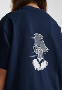 Mörkblå bomullströja med vit grafik av en hand i handsk och skridskor på baksidan, med en slät textur och avslappnad passform.