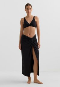 Črni bikini zgornji del z zasukanim središčem, kombiniran z visokim črnim krilom z odprtino in vozelnim poudarkom. Mehka tekstura tkanine.