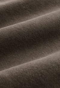 Közelkép puha, sötét, szürkésbarna anyagról, finom átlós twill szövésmintával és enyhe hajtásokkal, amelyek árnyékokat vetnek.