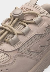 Bež sportska cipela s mrežastim i antilop panelima, elastičnim vezicama s okruglim klinom za zatvaranje i imenom robne marke "Hi-TEC" na jeziku.