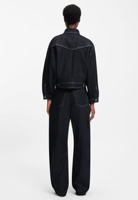 Tumša džinsa jaka un plats piegriezums bikses ar kontrastējošu šuvju izcelšanu, pogu dekorācijām un brīvu piegriezumu. Aizmugures skats atklāj piemērotas šuves un kabatas.