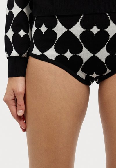 Os calções de malha em preto e branco apresentam um padrão de corações e formas de diamante, com uma textura suave e uma cintura em contraste.