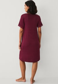 Camicia da notte bordeaux con maniche corte, caratterizzata da pizzo ai bordi delle maniche, un taglio rilassato e un design lungo fino al ginocchio. Texture morbida.