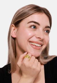 Goldener Mehrfachring mit einer glatten, polierten Oberfläche. An einer Hand mit heller Haut getragen. Der Hintergrund ist rein weiß.