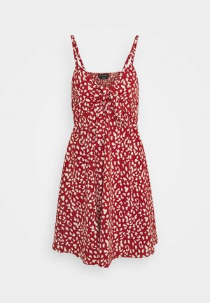 Czerwona sukienka bez rękawów z nieregularnymi białymi plamami, dopasowanym gorsetem, ozdobą na przodzie związaną na kokardę oraz rozkloszowanym dołem.