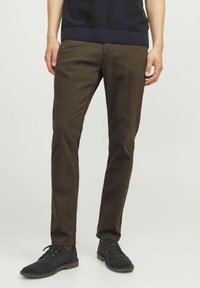 Pantaloni in cotone color marrone a taglio slim, con una texture liscia e design a cinque tasche, abbinati a scarpe in suede nere e a un maglione blu navy.