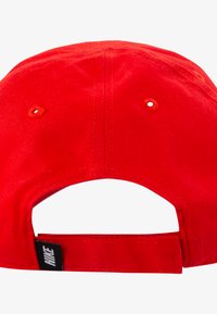 Rød bomullsbaseballcap med buet skygge og justerbar stropp bak, med ventilasjonshull og kontrasterende svart lapp.