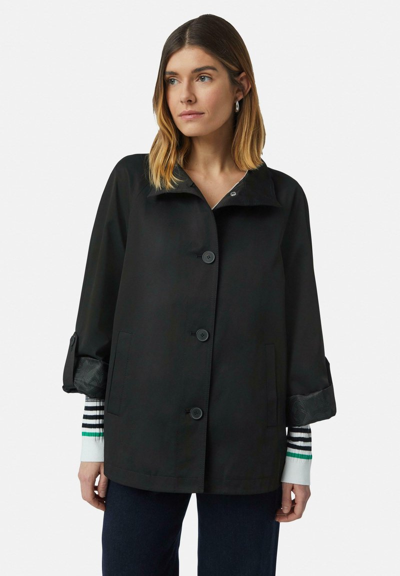 Schwarze Jacke mit einem breiten Kragen, großen Knöpfen und langen Ärmeln. Die Ärmel haben gemusterte Manschetten, die einen gestuften Look erzeugen.