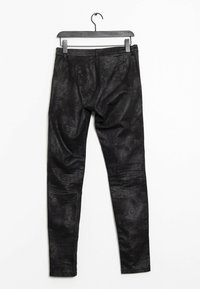 Černé legíny vyrobené z texturovaného materiálu, s jemným vzorem, hladkým povrchem, úzkým střihem a pasem. Visí na černém háčku.