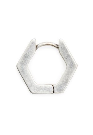 Pequeño pendiente de aro hexagonal plateado con cierre de alambre delgado y curvado sobre fondo blanco.
