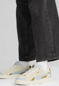 Crème en lichtblauwe sneakers met bruine accenten, van gestructureerd suède materiaal, ronde neuzen en witte veters, gecombineerd met zwarte wijde spijkerbroeken.