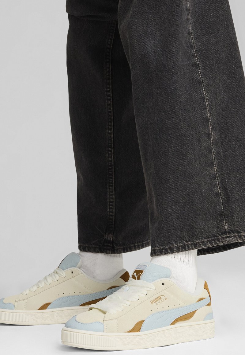Crème en lichtblauwe sneakers met bruine accenten, van gestructureerd suède materiaal, ronde neuzen en witte veters, gecombineerd met zwarte wijde spijkerbroeken.