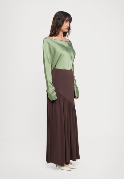 Grøn satin langærmet top i off-shoulder stil; brun maxiskørt med skrå plisseringer; lysfarvede spidse hæle.