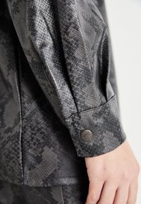 Schwarze und graue Schlangenprint-Fauxlederjacke mit einem Detail an den Knopfmanschetten und glatter Textur. Bietet eine lockere Passform und weichen Glanz.