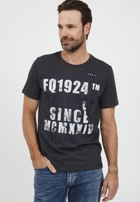 Tumehall T-särk, mis on valmistatud puuvillast, suure valge tekstiga, millel on "FQ1924" ja "SINCE MCMXXIV". Ümar kaelus ja lühikesed varrukad.